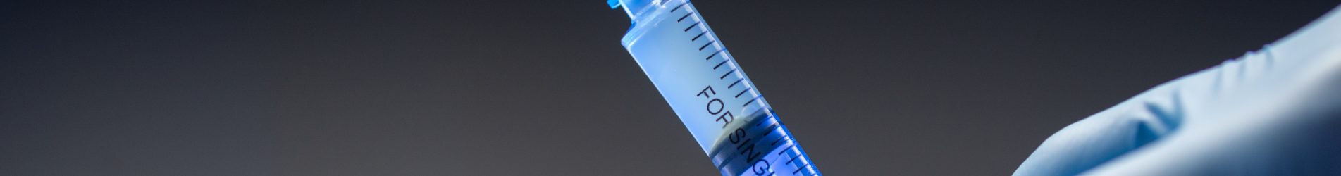 Hand in medical blue glove holding syringe. Grey background. Close-up vaccine vial dose. Medical concept vaccination, fight against virus covid 19 corona virus